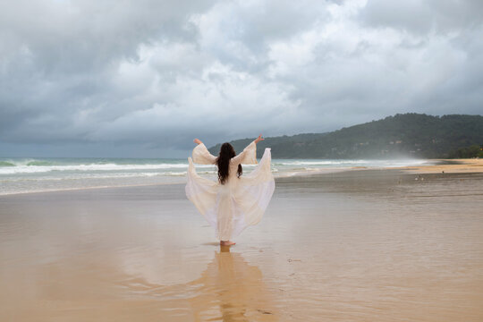 Back view young happiness asian traveller woman in white dress standing on beautiful sandy beach. Cute girl enjoy her tropical sea on relax holiday vacation during summer time