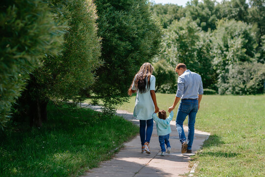 Happy African-American and European family walking and playing together in the park. Black family walking down the road holding hands