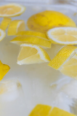 Juicy lemon slices with ice and water in a very cold pitcher on a yellow colored background, selective focus. Lemonade with a lot of lemon and ice top view