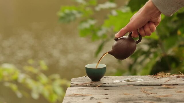 Close-up clay teapot pouring black tea into cup on Wooden Surface Outdoors