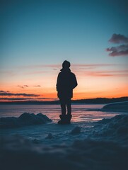 A silhouetted figure standing on a frozen lake during sunset, reflecting the beauty of nature and winter serenity.
