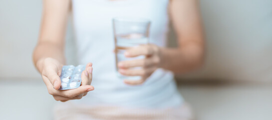 woman hand holding medicine painkiller pill and water glass on the sofa at home, taking for headaches, stomach ache, Diarrhea Pain from food poisoning, Endometriosis, Hysterectomy and Menstrual