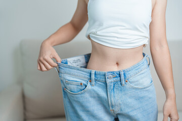 young slim female wearing big or oversize jeans, woman show healthy shape after weight loss....