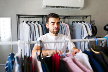 Male stylist choosing stylish garments in a trendy fashion store filled with customers looking for the latest menswear trends