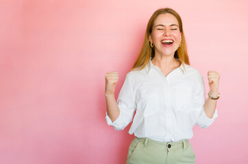 Young woman triumphantly raises her fists in the air against a vibrant pink backdrop