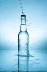 Water stream splashing on glass bottle with cap filled with water on wet reflective blue surface