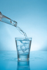 Glass bottle filling with water a glass glass with ice on wet reflective blue surface