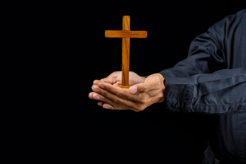 Man holding a wooden religion cross in his hand on black background. Symbol of faith and worship in God. People christianity prayer in church