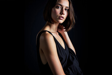 Naklejka premium Portrait of a woman in a black dress with short bob hairstyle in an elegant pose against a dark background with soft lighting