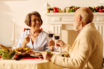 A senior couple shares a festive moment at home, toasting with glasses during Christmas dinner.