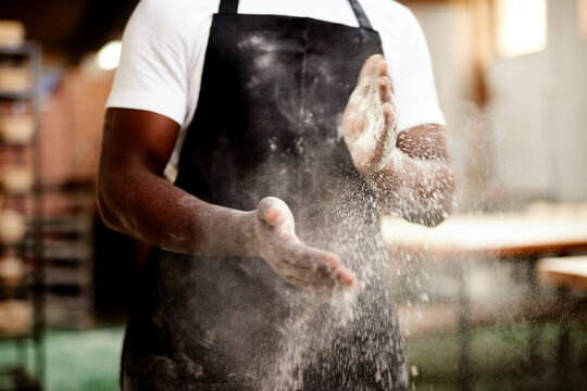 Black man, hands and dust with flour at bakery for bread, rolls or pastry production at factory. Closeup, male person or baker clapping powder or wheat for handmade ingredients or small business
