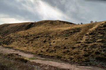 A scenic landscape featuring rolling hills under a dramatic sky. The winding dirt path adds depth to the view, making this outdoor setting perfect for nature lovers and those seeking peaceful scenery.