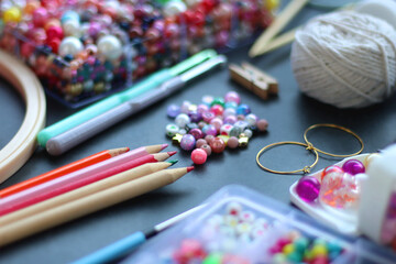 Colorful beads, coloring pencils, glitter, needles, string, hoop, tape and scissors on dark background. Various colorful craft supplies. Selective focus.