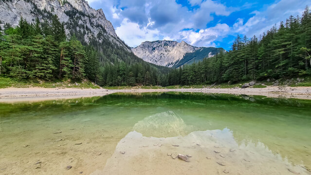 Serene alpine lake Gruener See reflects majestic mountain peak Messnerin, Hochschwab region, Styria, Austria. Wanderlust Austrian Alps. Clear water mirrors the towering ridges and lush idyllic forest