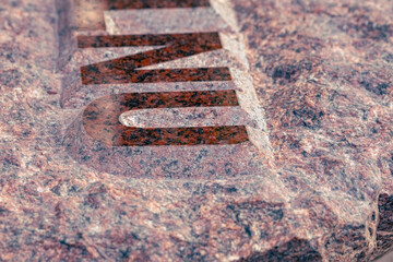 red granite stone with engraved raised hand made letters. Close up of a gravestone.