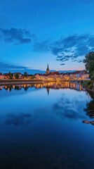 Fototapeta premium Illuminated cityscape reflected in calm water at dusk