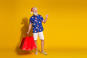 Full size photo of stylish modern santa shop bags direct finger empty space wear xmas winter print shirt isolated on yellow color background