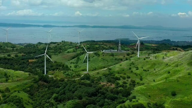 Aerial view of street on green hills with installed wind mills. Sea with islands during cloudy day in Philippines, Rizal Pililla. Wide shot.