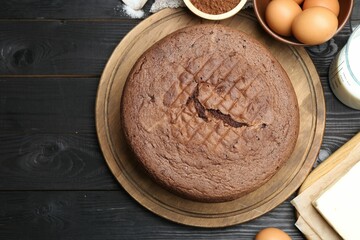 Tasty chocolate sponge cake and ingredients on black wooden table, flat lay