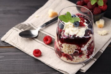 Tasty trifle dessert. Berries, sponge cake and whipped cream in glass on black wooden table