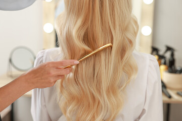 Professional hairdresser combing woman's hair in salon, closeup