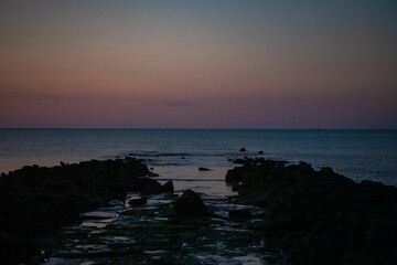 A beautiful, calm twilight scene characterized by gentle waves and a rocky shoreline at dusk, evoking peace