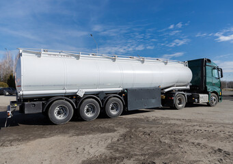 Green cab tractor semi-trailer with a specialized tank semi-trailer standing on the asphalt under a blue sunny sky Rear and side view