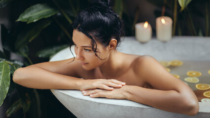 Serene young woman of Asian descent relaxes in a luxurious bathtub filled with citrus slices,...