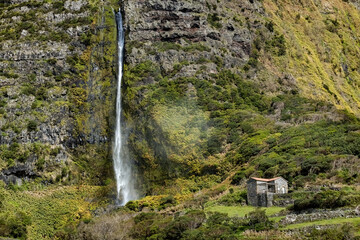 Small stone house in the mountains with waterfall next to it at Flores islamd Azores Portugal