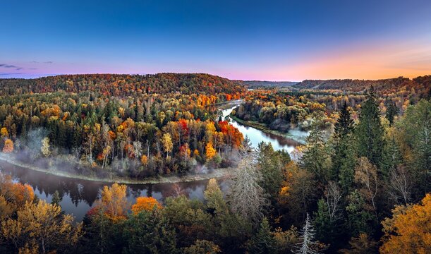 Colorful sunrise over the Gauja National park valley.  Sigulda city panorama from drone with forest in autumn colors.