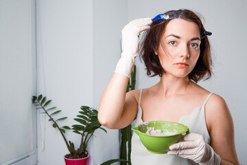 a woman dyes her hair at home on her own. Hands in dirty gloves in hair dye stretched out into the frame