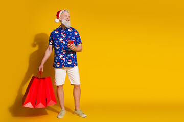Full size photo of stylish modern santa hold bags phone look empty space xmas winter print shirt isolated on yellow color background