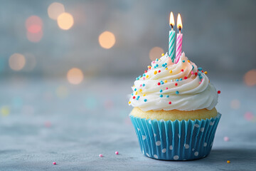 A cupcake with two candles on top of it. The candles are lit and the cupcake is decorated with sprinkles