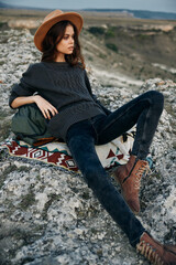 Serene woman in hat and sweater relaxes on blanket atop picturesque mountain summit