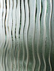 Frosted polycarbonate surface with metallic chrome reflections. Vertical ribbed patterns with abstract textured effect. Cool toned  icy palette. 