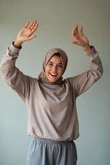 Happy woman in hijab raising hands, joyful expression, casual clothing, positive energy