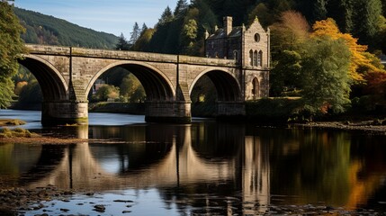 Fototapeta premium Stone Bridge Reflecting on Tranquil Waters, Amidst Autumnal Foliage and a Historic Structure