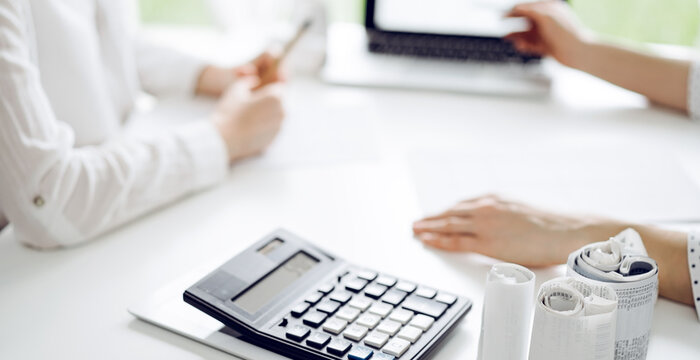 Calculator is lying at the white table near two female accounters counting taxes or making revenue balance. Business audit and finance concepts