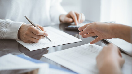 Woman accountant using a calculator and laptop computer while counting and discussing taxes with a client. Business audit concepts