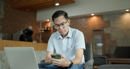 Businessman chatting on laptop. communication technology. Asian Middle-aged man using smartphone to...