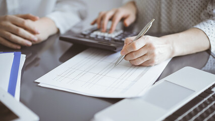 Woman accountant using a calculator and laptop computer while counting taxes for a client. Business...