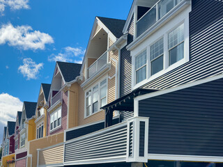 Street view of adjoined row of wooden residential houses with peaked roofs, patios, balconies, glass windows, white trim, and asphalt shingles. The townhouses are painted blue, yellow, red, and orange