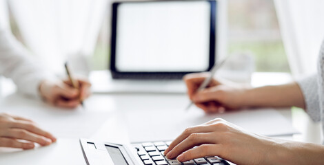 Two accountants using a calculator and laptop computer for counting taxes at white desk in office. Teamwork in business audit and finance