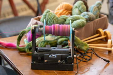 A woman uses an electric eel wheel to spin colorful pink wool into handspun textured yarn on a...