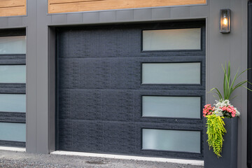 A modern black panel metal exterior garage doors with four small horizontal frosted glass windows....