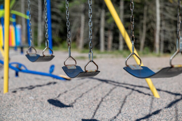 There are three school swings with black rubber seats hanging from metal chains. The children's...