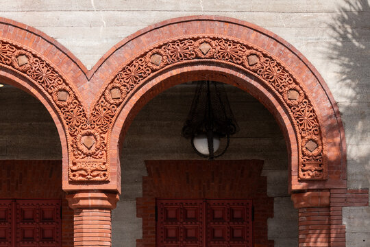 Two large red clay decorative exterior archways on a grey brick building. The vintage Spanish style architecture has decorative columns, trim and details in the arches.The opening leads to a courtyard - Powered by Adobe