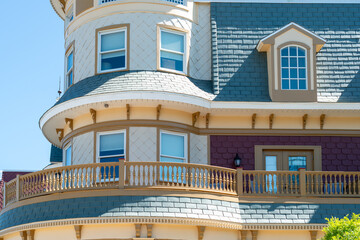 The exterior roof section of a blue, white, and yellow colored historic Victorian house with multiple windows, wrap-around patio, decorative molding, and fish scale shingles. The terret is octagon. © Dolores  Harvey