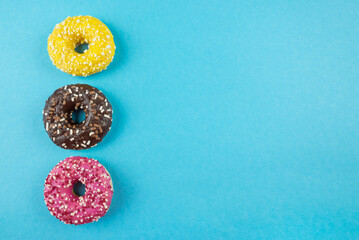 Three donuts with different glazes on a blue background with copy space. Place for text, banner.