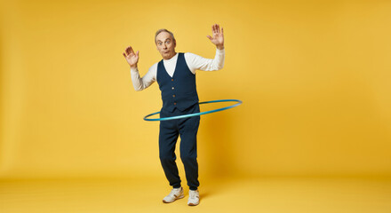 Cheerful senior man hula hooping in vibrant yellow studio for fitness and fun